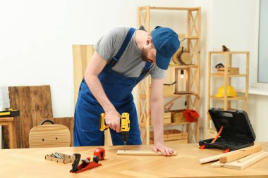 Sanatçı atölyedeki ahşap masada matkapla çalışıyor.