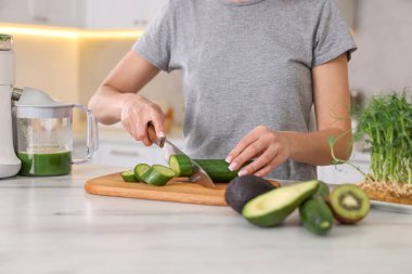 Mutfaktaki beyaz mermer masada salatalık kesen kadın, yakın plan.