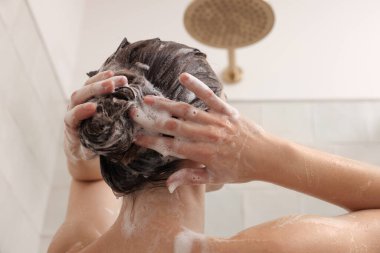 Woman washing hair while taking shower at home, back view