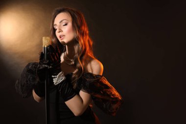 Koyu arka planda mikrofonlu şık elbiseli güzel bir kadın, mesaj için yer var.