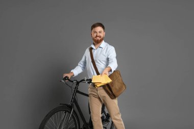 Bisikletli postacı gri arka planda mektupları teslim ediyor.