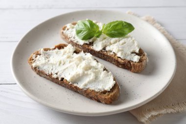 Beyaz ahşap masa üzerinde ricotta peyniri ve fesleğen, yakın plan