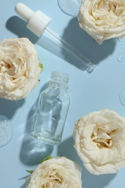 Güzel gül çiçekleri, kozmetik şişesi, pipet ve serumun damlaları açık mavi arka planda, düz yatıyordu.