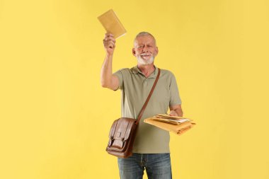 Kahverengi çantalı mutlu postacı sarı arka planda mektuplar getiriyor.