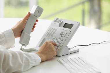 Assistant dialing number on telephone against blurred background, closeup