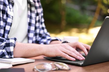 Dışarıdaki tahta masada dizüstü bilgisayarla çalışan Freelancer, yakın plan. Uzak görev