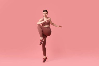 Genç bir kadın pembe arka planda aerobik egzersizi yapıyor.