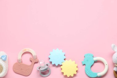 Renkli çıngıraklar ve soluk pembe arka planda emzik, metin için yeri olan düz bir yer. Bebek eşyaları.