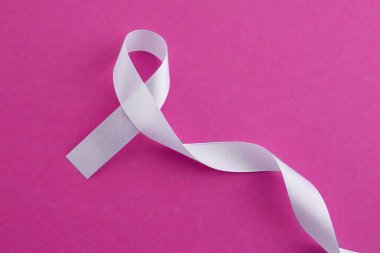 White awareness ribbon on pink background, top view