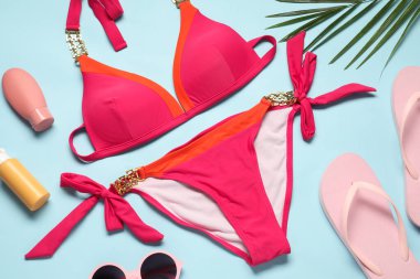 Güzel mayo, güneş kremi ve açık mavi arka planda parmak arası terlikleri olan düz bir kompozisyon.