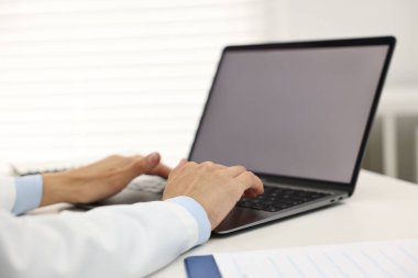 Hastanedeki beyaz masada dizüstü bilgisayar kullanan bir doktor.