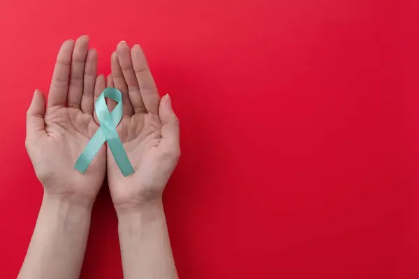 stock image Woman holding turquoise awareness ribbon on red background, top view. Space for text