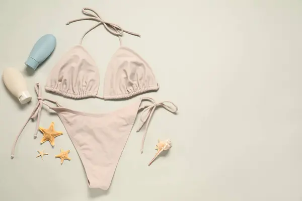 stock image Beautiful swimsuit, sunscreens and starfishes on beige background, flat lay. Space for text