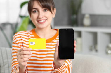 SIM kartı ve kapalı mekanda akıllı telefonu olan, seçici odaklı bir kadın. Metin için boşluk