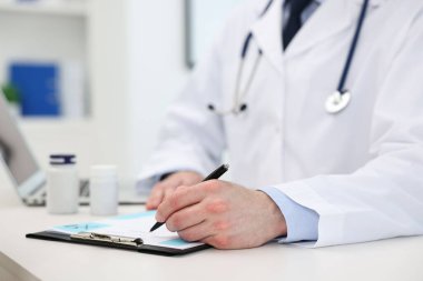 Klinikteki beyaz masada reçete yazan doktor, yakın plan.