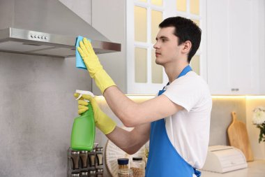 Profesyonel hademe üniformalı, mutfak kaputunu paçavra ve deterjanla temizliyor.