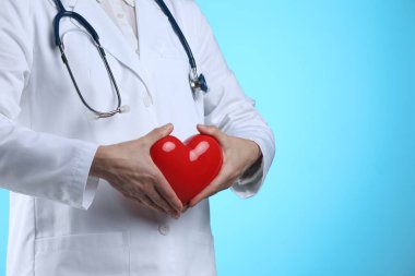 Açık mavi arka planda kırmızı kalpli doktor, yakın plan. Metin için boşluk