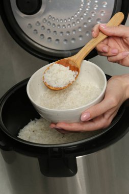 Gri arka planda kaynamış pirinci kaseye koyan kadın, yakın plan.