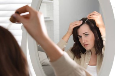Saç dökülme problemi. Kadın evdeki aynanın yanındaki saç çizgisine serum sürüyor.