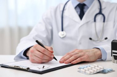 Klinikteki beyaz masada reçete yazan doktor, yakın plan.