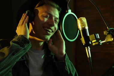 Profesyonel kayıt stüdyosunda mikrofona şarkı söyleyen kulaklıklı bir vokalist.