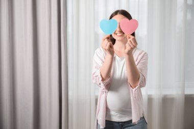 İkiz bekliyor. Evde iki tane kalp kesiği tutan hamile bir kadın. Mesaj atmak için yer var.