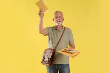 Kahverengi çantalı postacı sarı arka planda mektupları teslim ediyor.