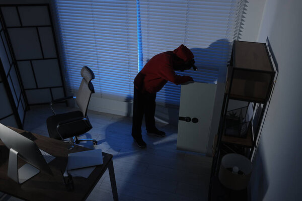 Вор с фонариком, ищущий деньги в офисе ночью, с видом сверху. Воровство