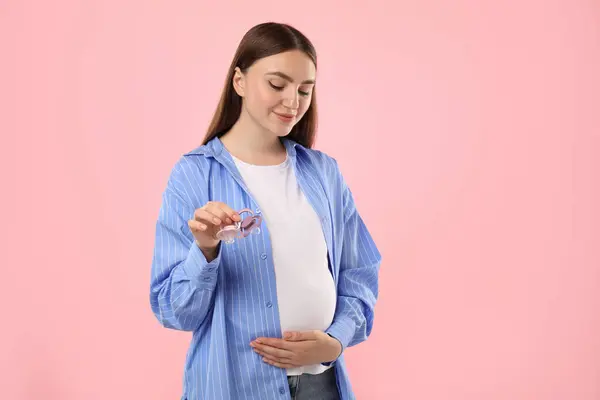 stock image Expecting twins. Pregnant woman holding two pacifiers on pink background, space for text