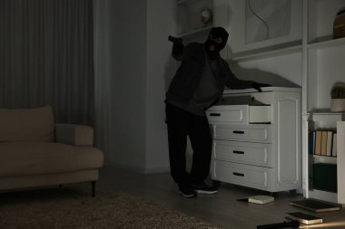Yabancı evde çekmecelerin yanında silahlı bir hırsız var. Düşük açılı. Hırsızlık.