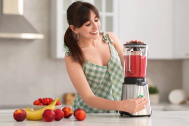 Genç bir kadın mutfaktaki beyaz mermer masada blender ile nefis smoothie yapıyor.