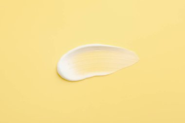 Sarı arka planda yüz kremi örneği, üst görünümde.