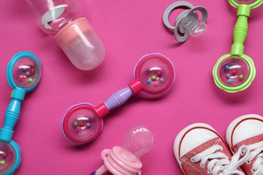 Renkli çıngıraklar, şişe, bebek ayakkabıları ve pembe arka planda emzikler.