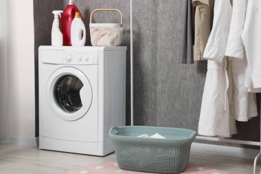 Çamaşır makinesi, deterjanlar, sepetler ve giysi rafları içeride.