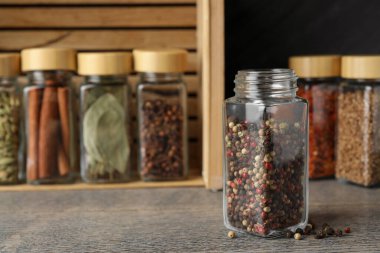 Cam kavanozdaki biberler ve gri ahşap masadaki diğer baharatlar, yakın plan.