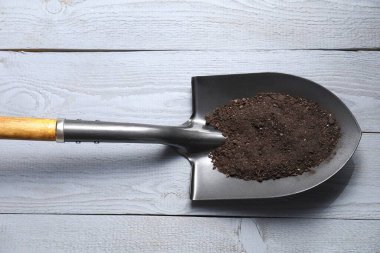 Açık gri ahşap masa üzerinde toprağı olan metal kürek, üst manzara.