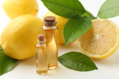Şişe, limon ve yeşil yaprakları beyaz masa üzerinde gerekli yağlar