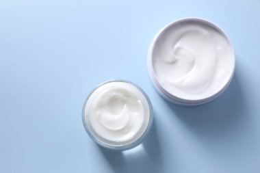 Açık mavi arka planda kavanozlarda yüz kremi, düz yatış. Metin için boşluk