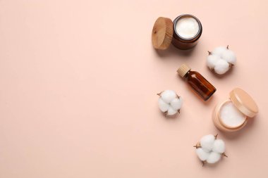 Farklı kozmetik ürünleri ve bej arka planda pamuk çiçekleri. Metin için boşluk