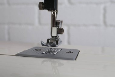 Modern dikiş makinesi beyaz tuğla duvara karşı, yakın plan.
