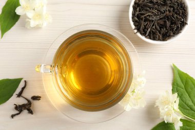 Sıcak yasemin çayı fincanda ve çiçekler beyaz ahşap masada, düz yerde.