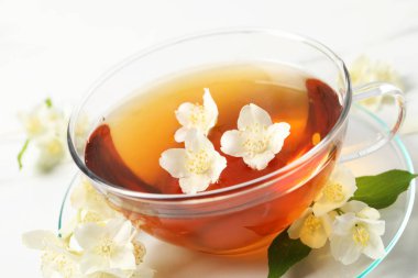 Sıcak yasemin çayı fincanda ve çiçekler beyaz mermer masada, yakın plan.