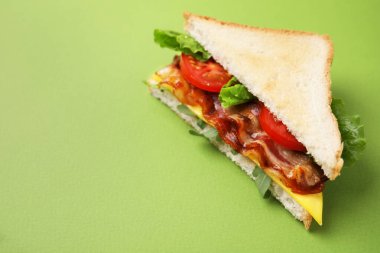 Yeşil arka planda kızarmış pastırmalı lezzetli sandviç, yakın plan. Metin için boşluk
