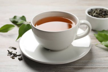 Yeşil çayı fincanda tazeleyen ve gri ahşap masada yapraklar, yakın plan