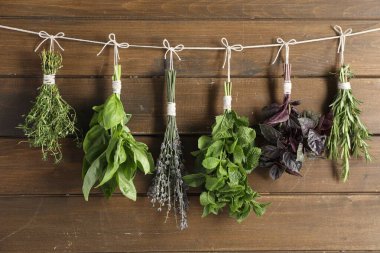 Ahşap duvarın yanında ipte asılı farklı aromatik otlar var.