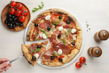 Kızarmış jambon, zeytin, mozzarella peyniri ve roka eşliğinde hafif ahşap masada lezzetli bir pizza yiyen bir kadın.