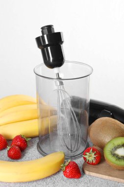 El blender seti, taze meyve ve çilek gri masada beyaz arka planda.