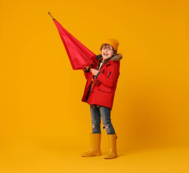 Turuncu arka planda kırmızı şemsiyeli küçük çocuk