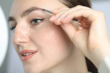 Genç bir kadın cımbızla kaş yoluyor arka planda, yakın plan