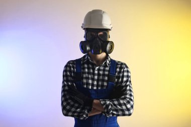 Gaz maskeli ve kasklı, kolları çapraz renkli bir işçi.